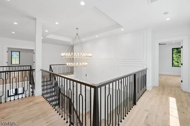 hall featuring a raised ceiling, a chandelier, light wood finished floors, and an upstairs landing