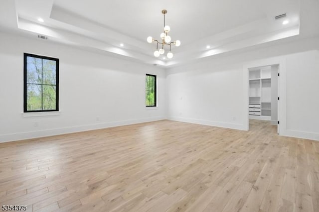 spare room with recessed lighting, a raised ceiling, light wood-type flooring, and a notable chandelier