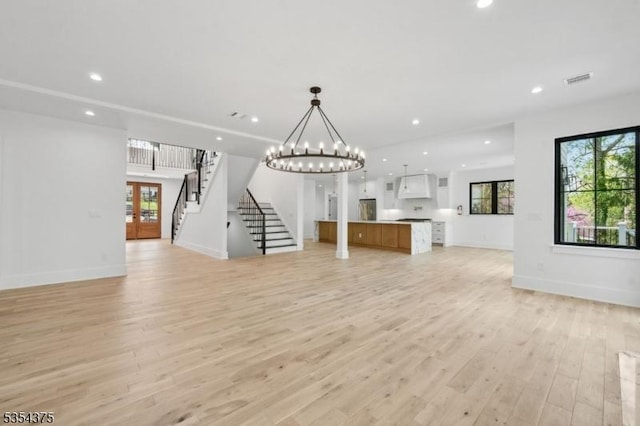 unfurnished living room with recessed lighting, light wood-style flooring, stairs, and an inviting chandelier