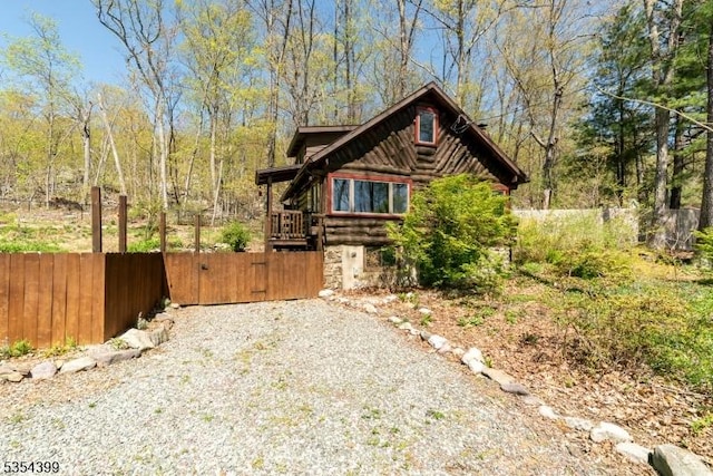 view of property exterior with driveway, fence, log siding, and a gate