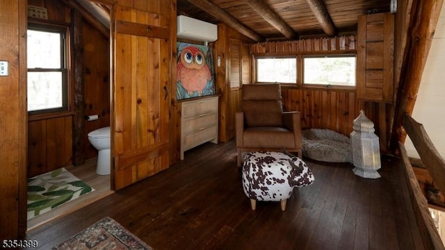 sitting room with a wall mounted air conditioner, wood walls, hardwood / wood-style floors, wooden ceiling, and beamed ceiling