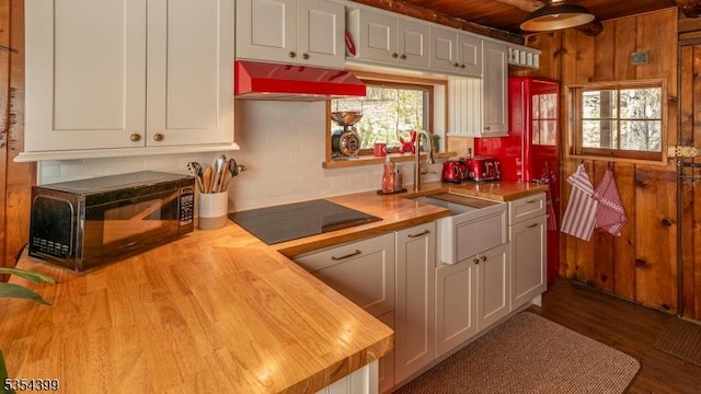 kitchen featuring butcher block counters, wood finished floors, range hood, white cabinetry, and black appliances