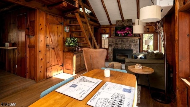 dining room with wood ceiling, a stone fireplace, wood finished floors, lofted ceiling with beams, and wooden walls