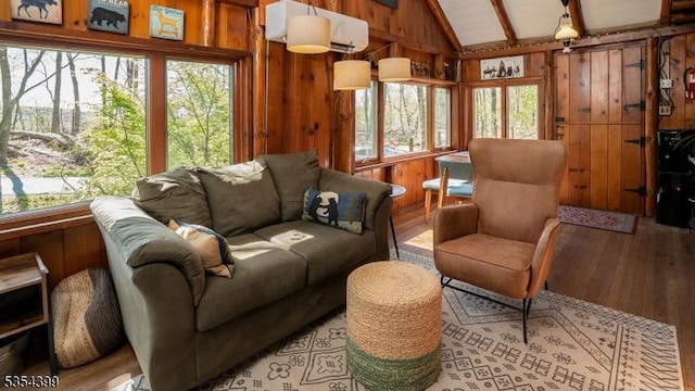 interior space with wooden walls, lofted ceiling with beams, light wood-type flooring, and a wall unit AC