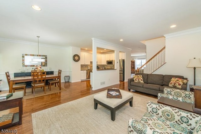 living room with stairs, recessed lighting, ornamental molding, and light wood-style flooring