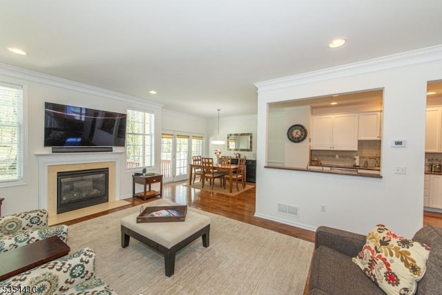 living room featuring visible vents, a fireplace with flush hearth, wood finished floors, and a wealth of natural light