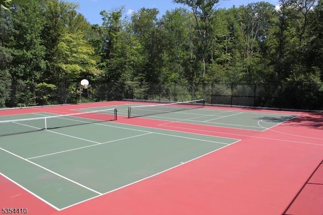 view of tennis court with a forest view, community basketball court, and fence