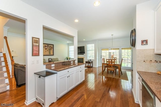 kitchen with white cabinets, crown molding, hanging light fixtures, a fireplace, and dark wood finished floors