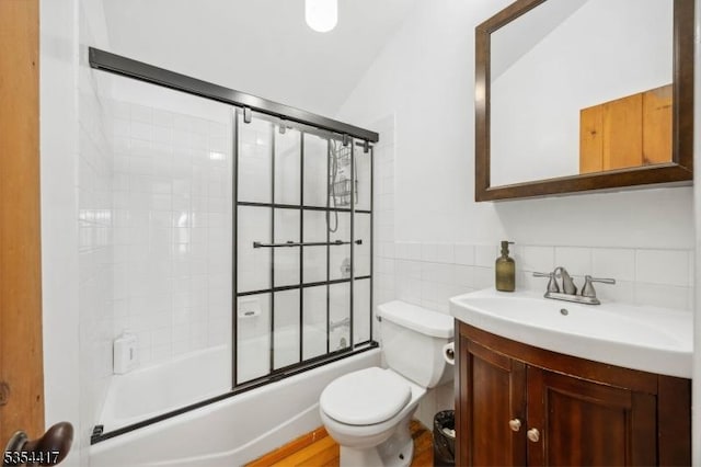 full bathroom with vanity, bath / shower combo with glass door, toilet, and tile walls