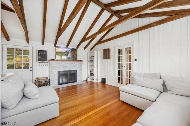 living area with a stone fireplace, wood finished floors, and vaulted ceiling with beams