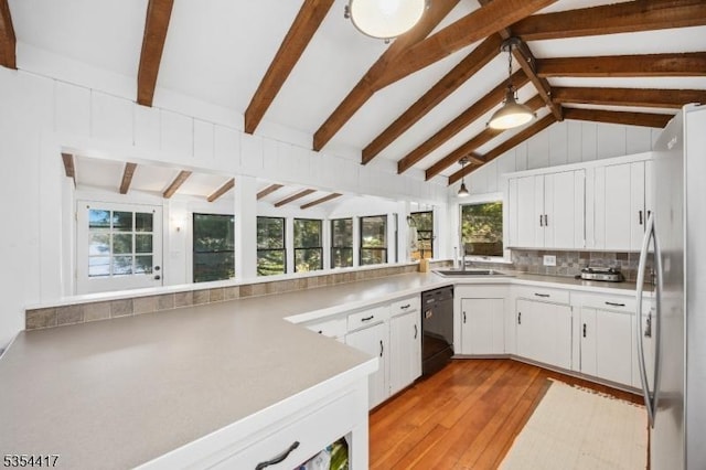 kitchen with lofted ceiling with beams, a sink, dishwasher, freestanding refrigerator, and tasteful backsplash