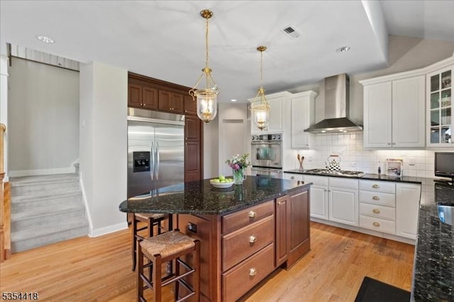 17 Hunters Path, Montgomery Twp, NJ 08558 - kitchen featuring wall chimney range hood, light wood-type flooring, a center island, white cabinetry, and appliances with stainless steel finishes