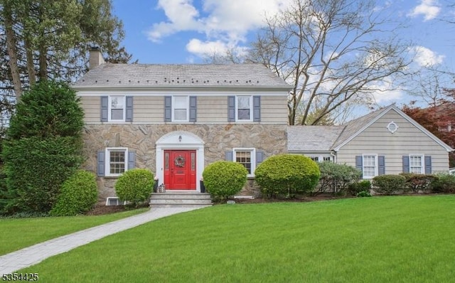 colonial inspired home featuring a high end roof, a chimney, a front lawn, and stone siding