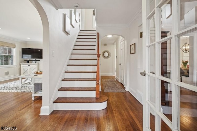 stairs with crown molding, arched walkways, and wood finished floors