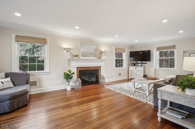 living area with crown molding, wood finished floors, visible vents, and a fireplace