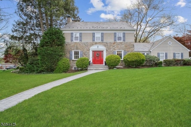 colonial house with a front yard, stone siding, and a chimney
