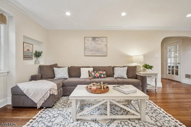 living room featuring arched walkways, wood finished floors, baseboards, ornamental molding, and recessed lighting
