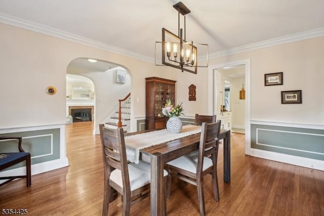 dining space with an inviting chandelier, ornamental molding, wood finished floors, stairway, and arched walkways