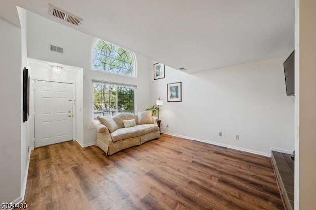 living area with baseboards, visible vents, wood finished floors, and a towering ceiling