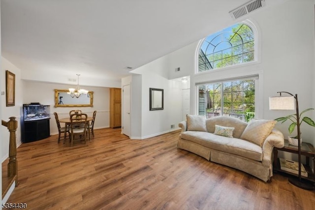 living area with visible vents, a towering ceiling, wood finished floors, baseboards, and a notable chandelier
