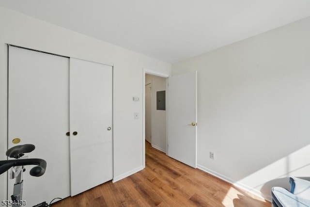 bedroom with a closet, baseboards, wood finished floors, and electric panel