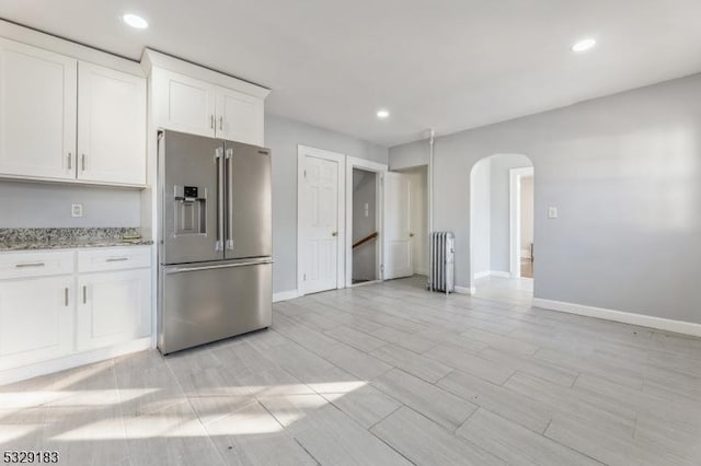 kitchen with arched walkways, light stone countertops, high end refrigerator, baseboards, and white cabinetry