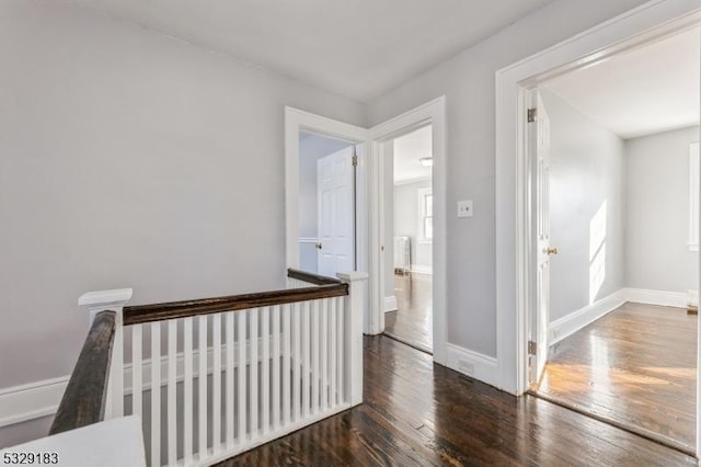 corridor featuring baseboards, hardwood / wood-style floors, and an upstairs landing