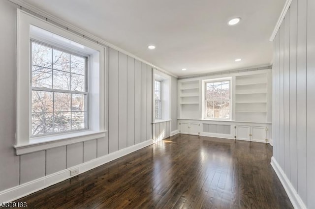 spare room with ornamental molding, a decorative wall, dark wood-style floors, and built in shelves