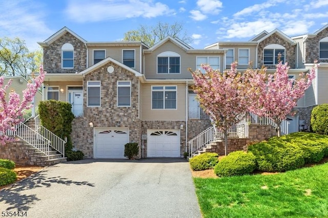 view of front of house featuring stairs, asphalt driveway, an attached garage, and stone siding
