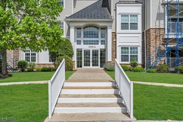 property entrance with french doors, a standing seam roof, stone siding, metal roof, and a yard