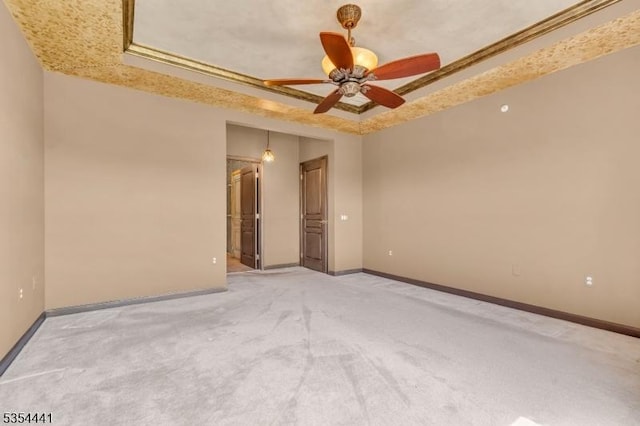 empty room featuring a tray ceiling, light colored carpet, and baseboards