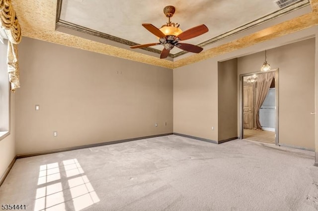 unfurnished room with a tray ceiling, light colored carpet, baseboards, and crown molding