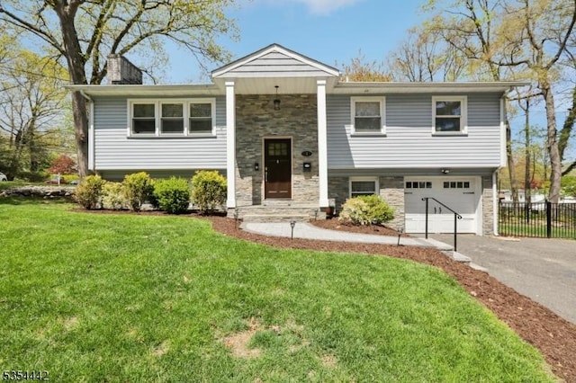 split foyer home featuring aphalt driveway, a garage, fence, a front lawn, and stone siding