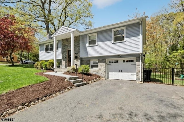 bi-level home featuring an attached garage, aphalt driveway, fence, and stone siding