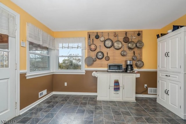 kitchen with stainless steel microwave, plenty of natural light, white cabinets, and baseboards