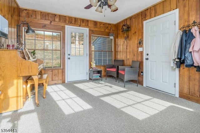 carpeted entryway featuring wood walls and a ceiling fan