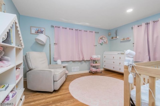 bedroom featuring wood finished floors, recessed lighting, a crib, and baseboards