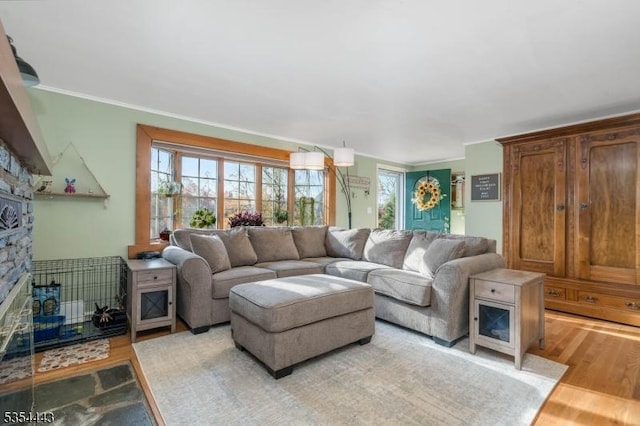living room featuring a stone fireplace, light wood-style flooring, and crown molding