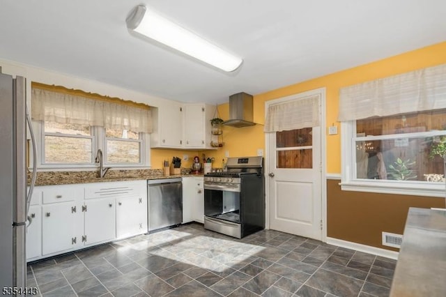 kitchen featuring appliances with stainless steel finishes, wall chimney range hood, a sink, and healthy amount of natural light