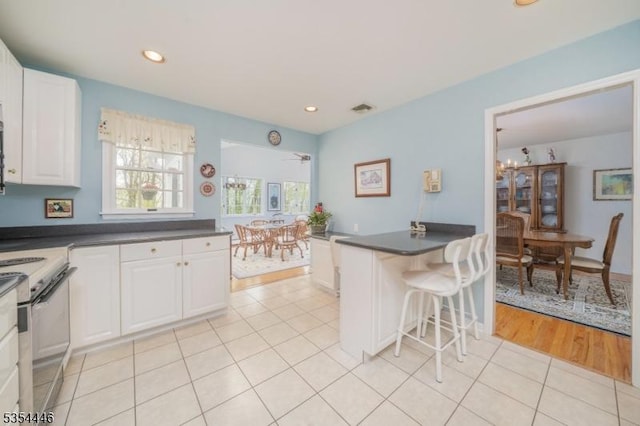 kitchen with light tile patterned floors, dark countertops, white cabinets, and white electric range
