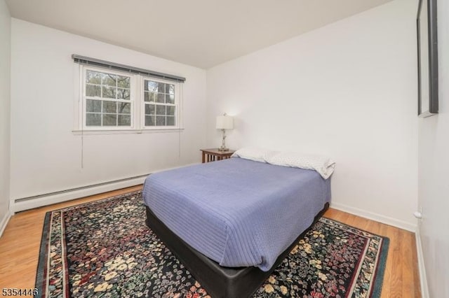 bedroom with baseboards, a baseboard heating unit, and wood finished floors