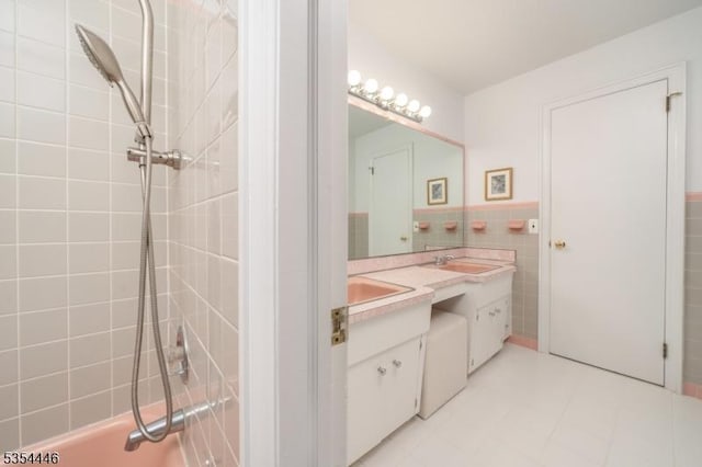 full bath with double vanity, a sink, a wainscoted wall, and tile walls