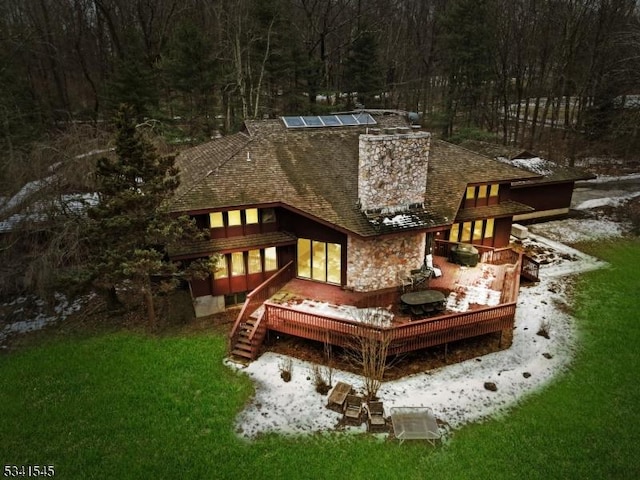 rear view of house featuring a deck, stairs, a shingled roof, a yard, and solar panels