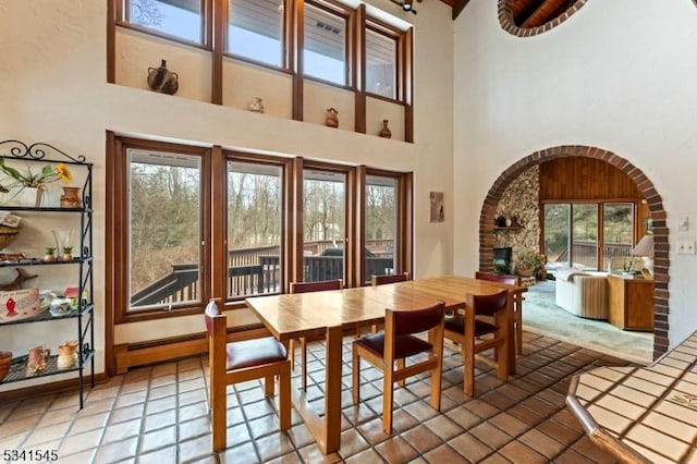 tiled dining room featuring baseboards, arched walkways, a high ceiling, and a large fireplace