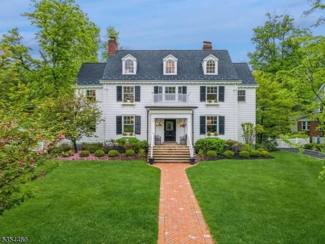 colonial inspired home with a chimney, a front yard, and a balcony