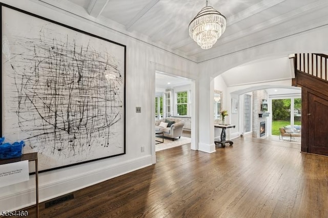 entrance foyer with arched walkways, wood finished floors, a chandelier, baseboards, and a large fireplace