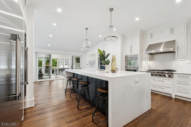 kitchen featuring appliances with stainless steel finishes, white cabinets, backsplash, wall chimney exhaust hood, and a center island