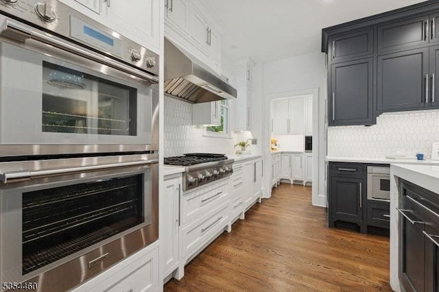 kitchen with stainless steel appliances, light countertops, under cabinet range hood, decorative backsplash, and dark wood-type flooring