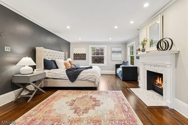 bedroom featuring crown molding, dark wood finished floors, a fireplace, baseboards, and recessed lighting