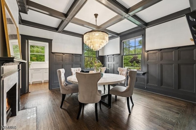 dining area with a decorative wall, coffered ceiling, a chandelier, dark wood-type flooring, and a premium fireplace